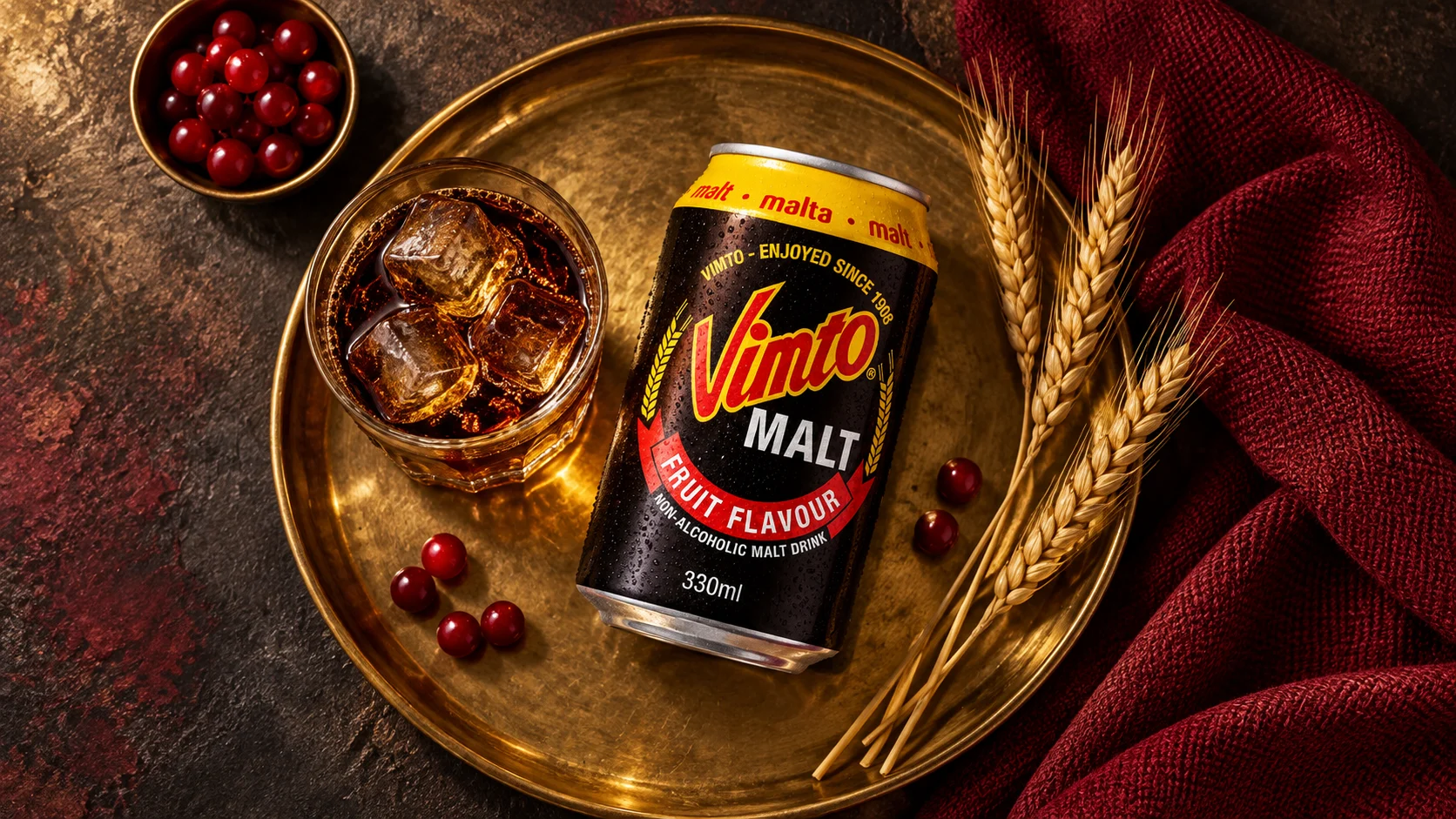 Vue de dessus d'une canette Vimto Malt, d'un verre et d'épis de blé sur un plateau doré.